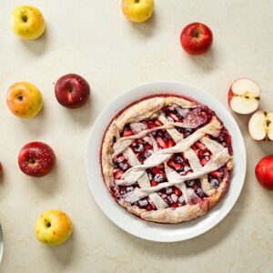 Delicious homemade apple pie with lattice crust surrounded by fresh apples on a marble surface.
